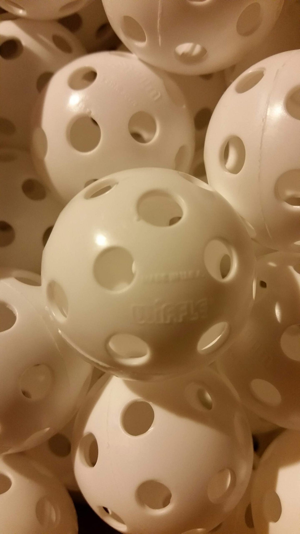 WIFFLE ball in hand shows perforations for safe indoor/outdoor use.